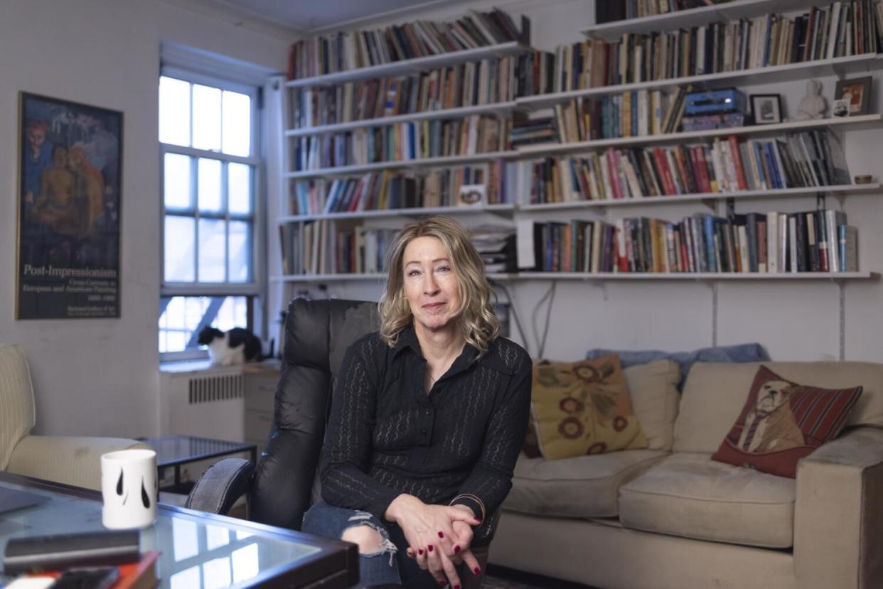 A woman sits on a couch in front of full bookshelves in a Manhattan apartment