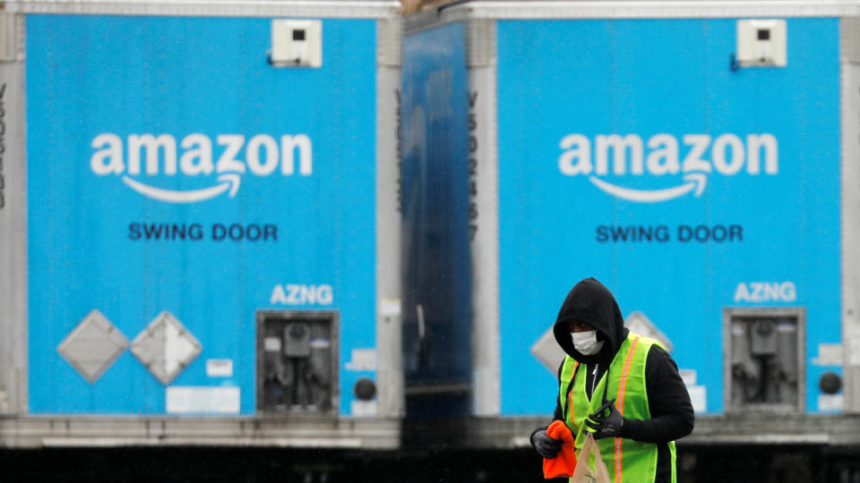 A worker in a face mask walks by trucks parked at an Amazon facility as the global coronavirus outbreak continued in Bethpage on Long Island in New York, U.S., March 17, 2020. REUTERS/Andrew Kelly