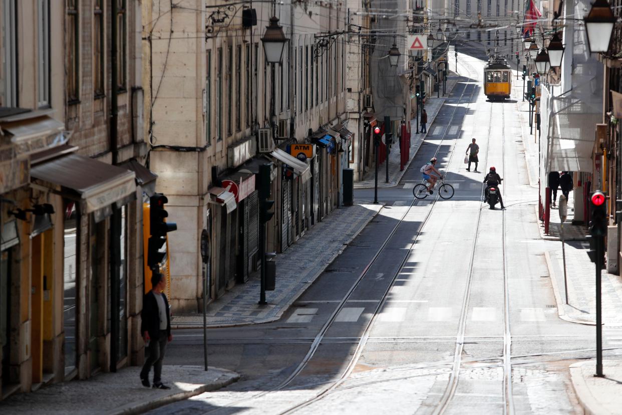 A few people walk on a street nearly empty of traffic in downtown Lisbon, Portugal on Friday, April 10, 2020.