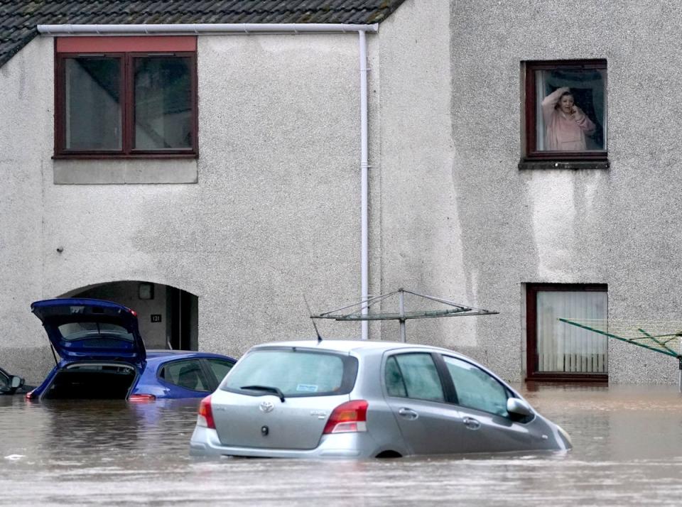 A person looks from a window at a submerged car in flood water in Brechin, Scotland, (PA)