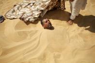 A worker stands next to a patient buried in the hot sand in Siwa, Egypt, August 12, 2015. (REUTERS/Asmaa Waguih)