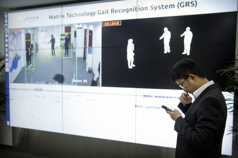 In this Oct. 31, 2018, photo, Huang Yongzhen, CEO of Watrix, checks his smartphone as employees demonstrate the use of their firm's gait recognition software at his company's offices in Beijing. A Chinese technology startup hopes to begin selling software that recognizes people by their body shape and how they walk, enabling identification when faces are hidden from cameras. Already used by police on the streets of Beijing and Shanghai, “gait recognition” is part of a major push to develop artificial-intelligence and data-driven surveillance across China, raising concern about how far the technology will go. (AP Photo/Mark Schiefelbein)