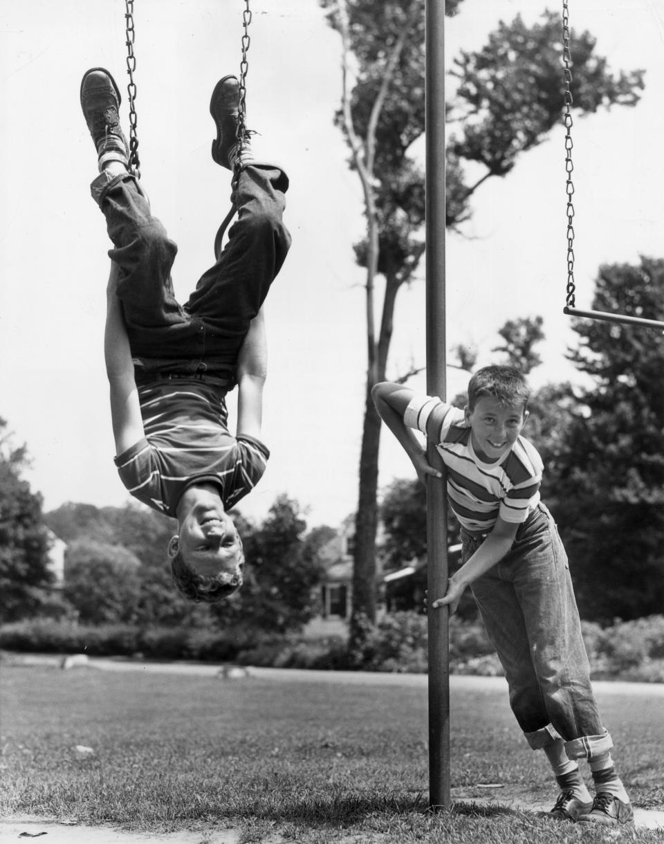 Circa 1945:  One young boy hangs upside down on the rings of a playground swing set, as another boy leans against a pole next to him.  (Photo by Lambert/Getty Images)