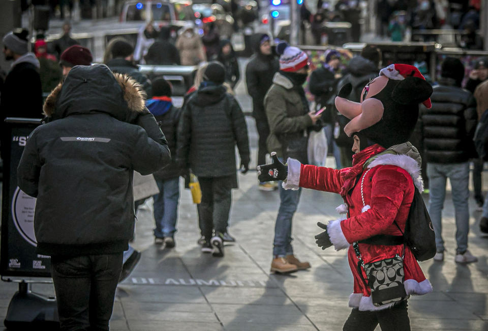 In this Thursday, Dec. 19, 2019 photo, a costumed character, right, tries to convince a passerby to stop and snap photos together for money, in Times Square, N.Y. Complaints about the sometimes aggressive behavior of the performers prompted the city in 2016 to passed a law relegating the Times Square characters to 8-by-50 foot “activity zones" where they might annoy fewer people. (AP Photo/Bebeto Matthews)