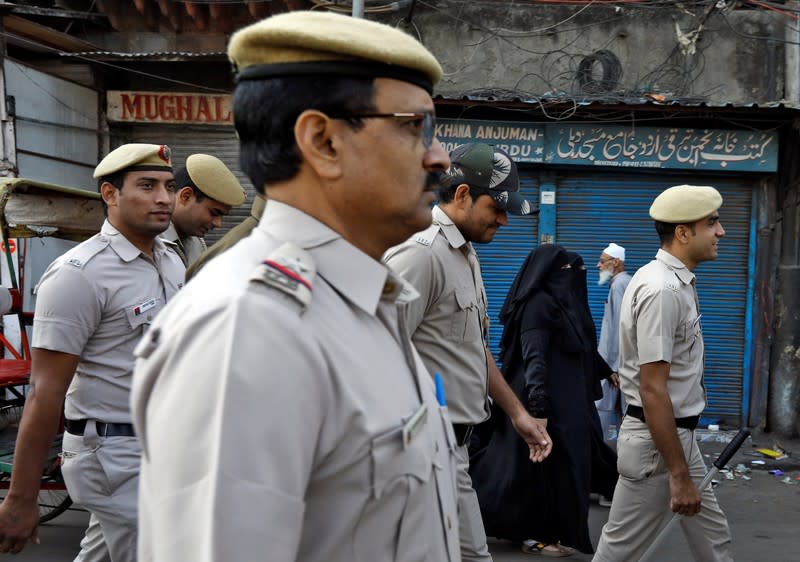 Veiled Muslim woman walk past police officers conducting a flag march in a street outside Jama Masjid, before Supreme Court's verdict on a disputed religious site claimed by both majority Hindus and Muslim in Ayodhya, in Delhi