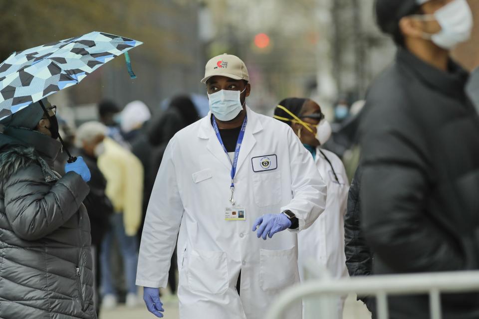 A medical worker walks past people lined up at Gotham Health East New York, a COVID-19 testing center Thursday, April 23, 2020, in the Brooklyn borough of New York. (AP Photo/Frank Franklin II)