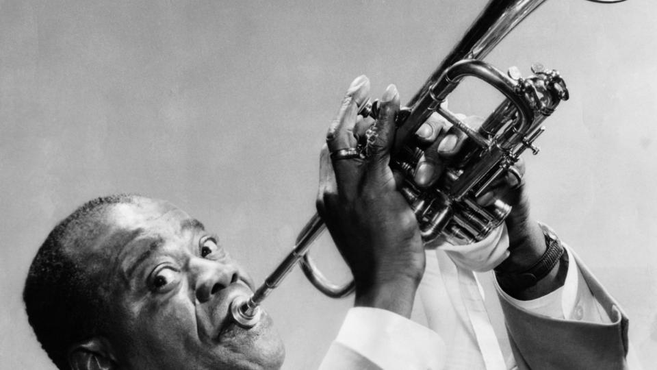 louis armstrong looking ahead toward a camera as he plays a trumpet