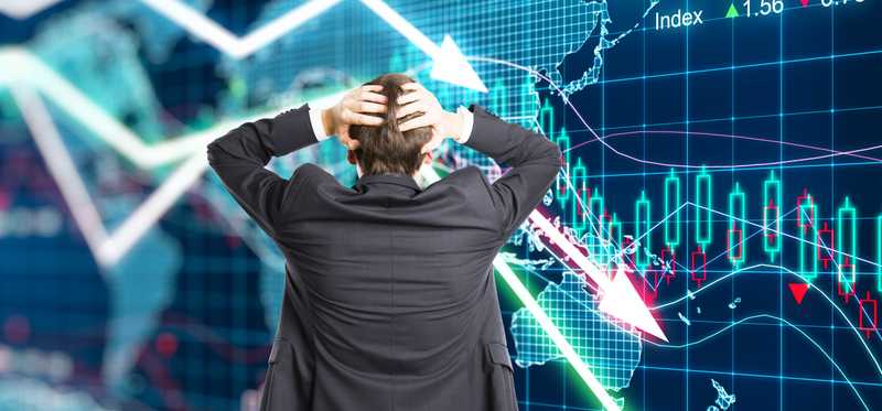 Man in suit holds his head while looking at plunging line graphs.