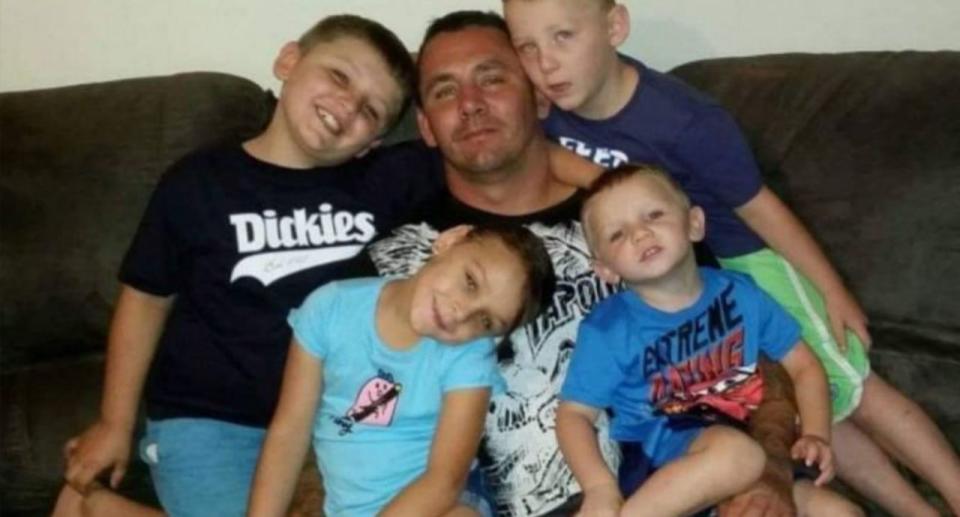 Mark Keans' with a suntan pictured with his four young sons in a variety of multi-coloured t-shirts sat on a brown sofa. 