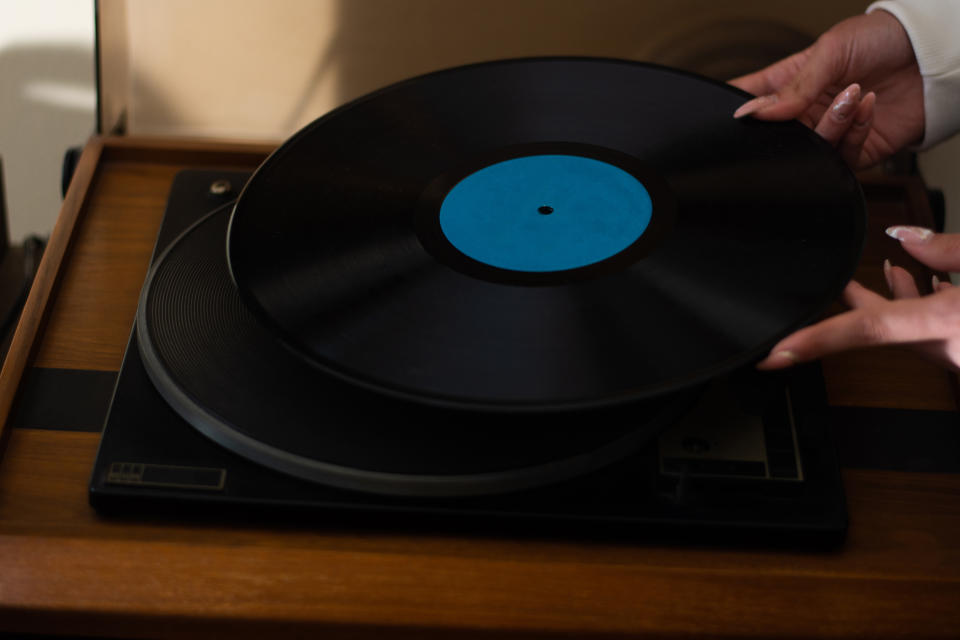 Hands are shown placing a vinyl record on a turntable