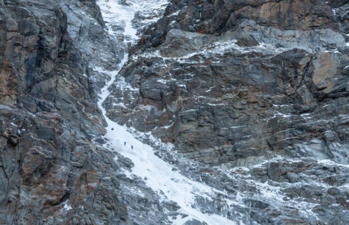 The clibmers heading up a snow couloir between rocky walls