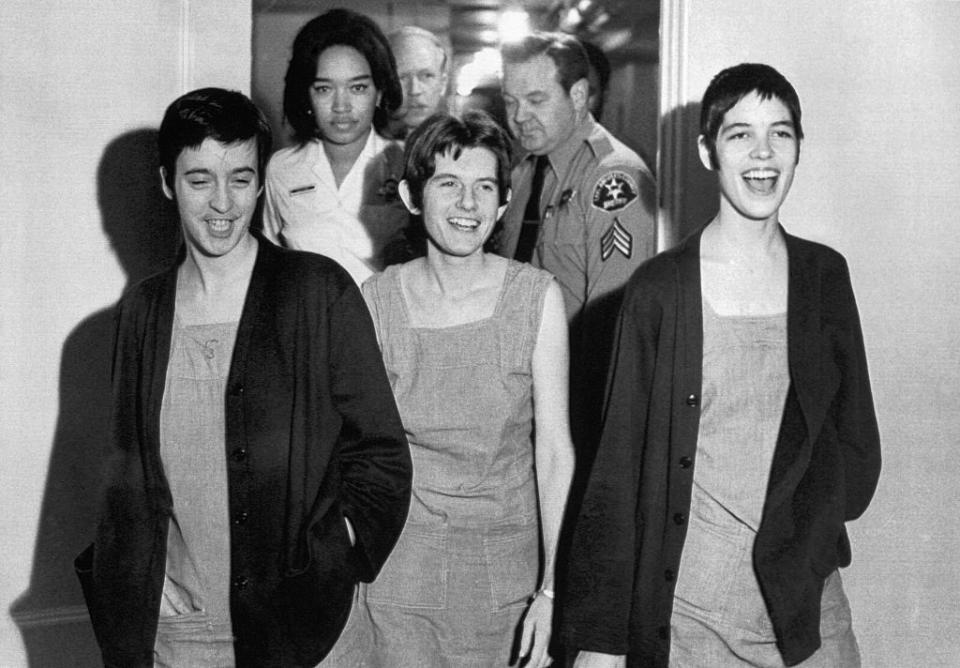 three women walking out of a courtroom laughing, while other people follow them from the doorway