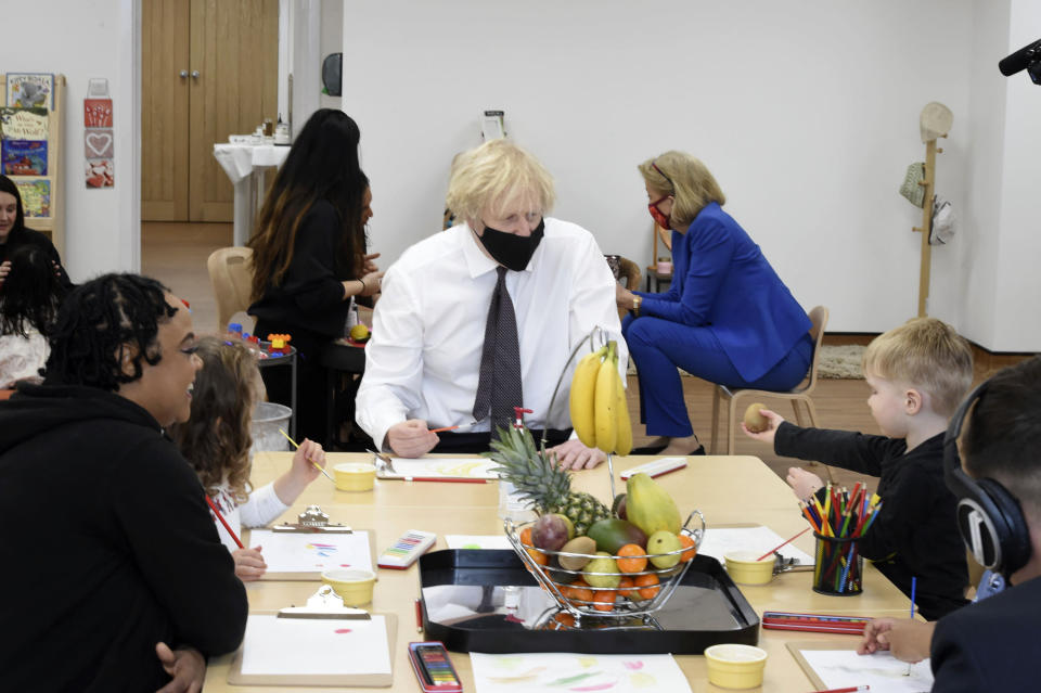 British Prime Minister Boris Johnson, center, sits with children drawing of a bunch of bananas during a visit to the Monkey Puzzle Nursery in Greenford, west London, Thursday, March 25, 2021. (Jeremy Selwyn/Pool Photo via AP)