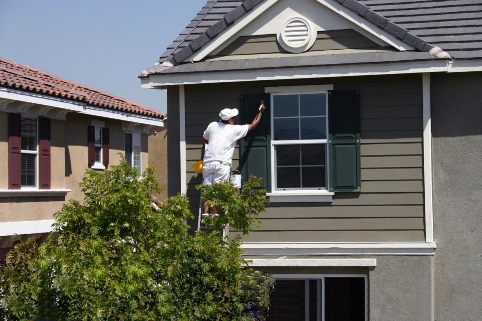 A worker in white paints window shutters.