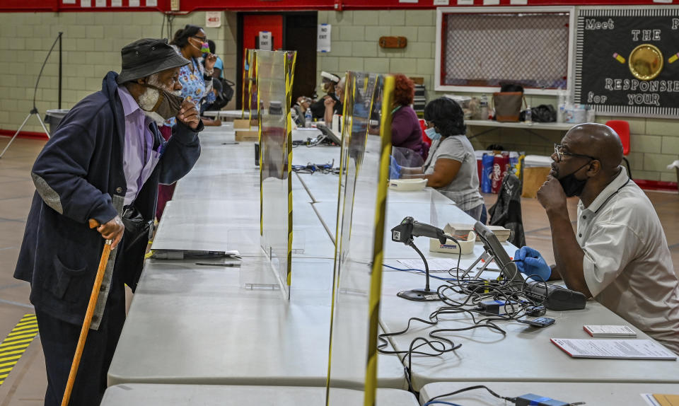 Voter Wayne Polston, left, has to briefly lower his mask in order to be understood by an election judge at Edmondson Westside High School during the primary election in Baltimore, Tuesday, June 2, 2020. (Jerry Jackson/The Baltimore Sun via AP)