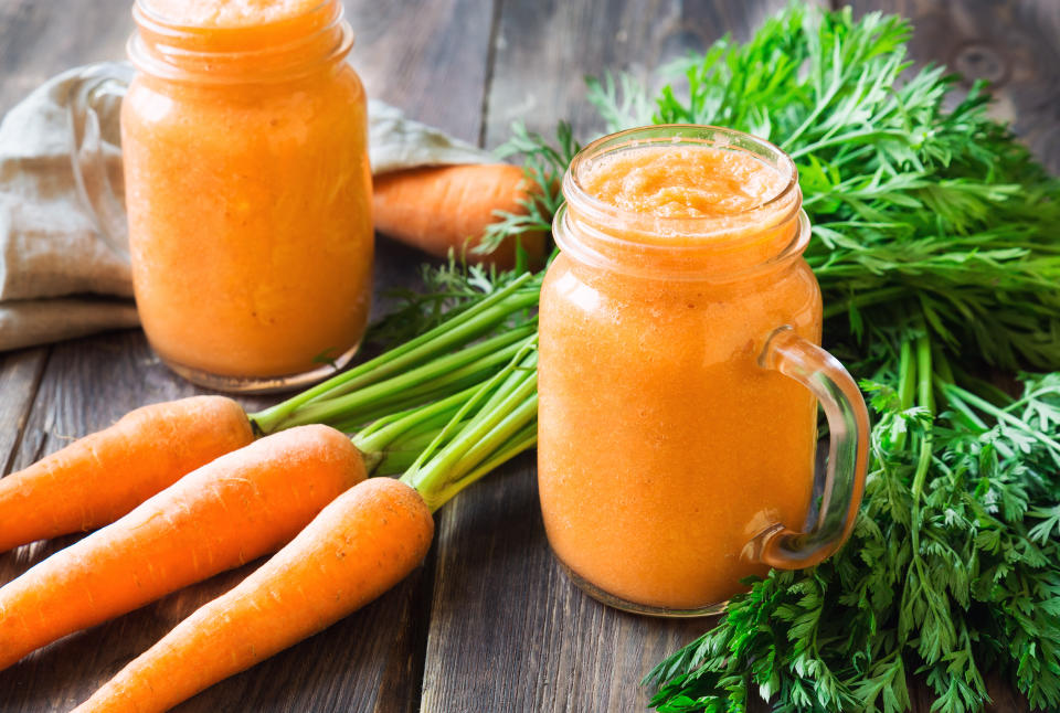 Carrots and carrot juice sitting on a wooden table. (Photo via Getty Images)