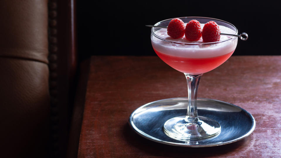 Clover Club Cocktail, a Sour Drink with Gin, Raspberries, and Egg White Foam in a Dark Luxurious Bar with Copy Space