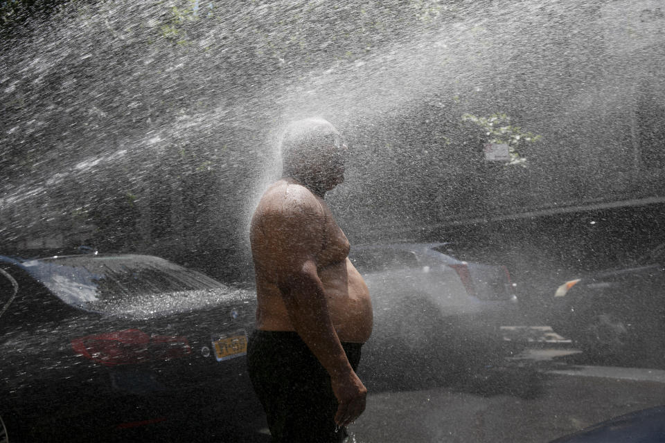 FILE - In this Tuesday, July 28, 2020 file photo, Rey Gomez cools off in the spray from a fire hydrant in New York, as the city opened more than 300 fire hydrants with sprinkler caps to help residents cool off during a heat wave. According to a study published Tuesday, May 25, 2021 in Nature Communications, during the summer of 2017 in nearly all large urban areas, people of color are exposed to more extreme urban heat than white people. (AP Photo/Mark Lennihan, File)