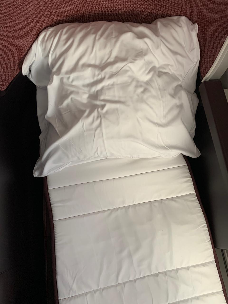 An airplane bed with white sheets and a white pillow.
