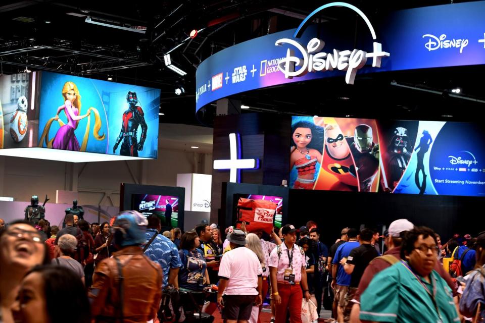 Crowds of people walk beneath lighted signs advertising Disney+.