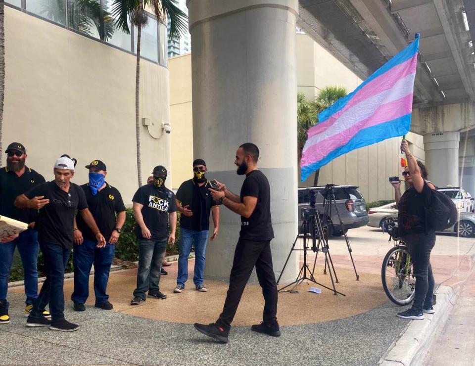 A person waving a transgender flag stands in front of a group of Proud Boys outside a contentious Miami-Dade School Board meeting, where recognizing LGBTQ+ History Month was discussed.