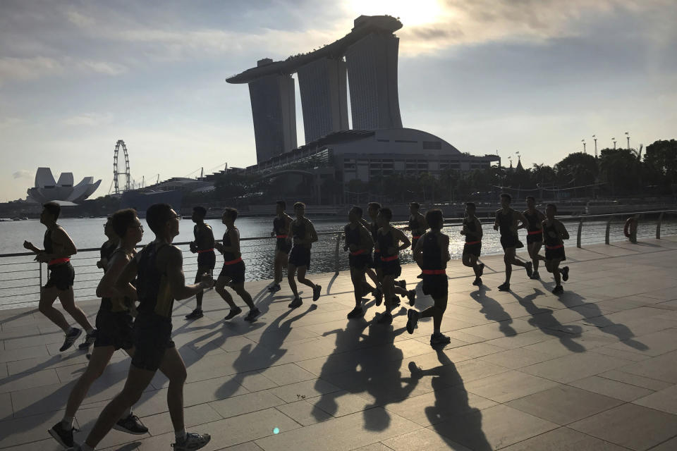 FILE - In this Aug. 4, 2017, file photo, runners are seen in silhouette and their shadows cast on the Marina Bay promenade as they jog at the start of a work day in Singapore. The Marina Bay Sands hotel towers, right, ArtScience Museum, left, and Singapore Flyer, second left, are seen in the background. On Wednesday, April 3, 2019, casino company Las Vegas Sands announced it'll spend $3.3 billion to expand its property in Singapore by adding an entertainment arena, another hotel tower and additional convention space. (AP Photo/Wong Maye-E, File)