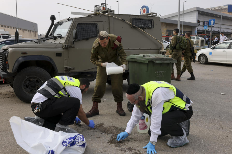 Members of Israeli Zaka Rescue and Recovery team and an Israeli soldier clean blood from the site of an attack, at the Ariel Industrial Zone, near the West Bank Jewish settlement of Ariel, Tuesday, Nov. 15, 2022. A Palestinian killed two Israelis and wounded four others in an attack in a settlement in the occupied West Bank on Tuesday before he was shot and killed by Israeli security personnel, Israeli paramedics and Palestinian officials said. (AP Photo/Oren Ziv)