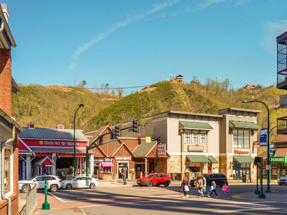 A sunny street with a multicolor buildings and mountains behind it. The sky behind is clear and blue