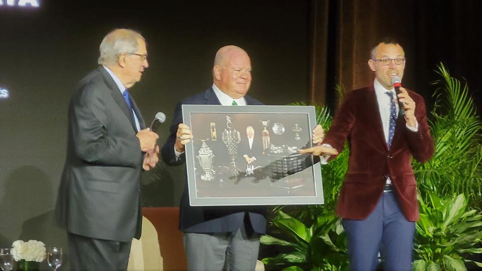 Race team owner Chip Ganassi (center) holds the autographed photo with concours founder Bill Warner as auctioneer Max Girardo seeks what ended up being a $22,000 bid.