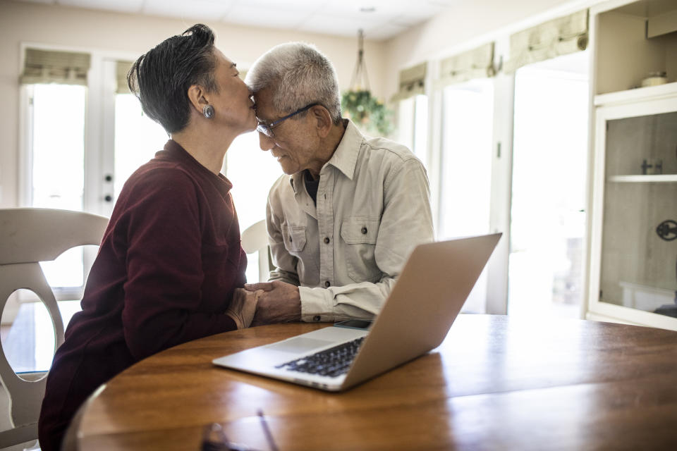 Older couple shares a loving kiss at a table with a laptop, manifesting affection