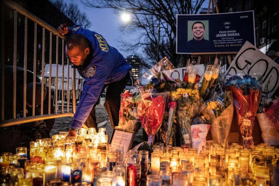 A New York City Police Department officer lights a candle at a makeshift memorial outside the New York Police Department's 32nd Precinct, near the scene of a shooting that claimed the lives of NYPD officers Jason Rivera and Wilbert Mora in the Harlem neighborhood of New York, Monday, Jan. 24, 2022.