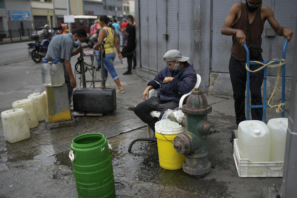 Residents tap into a fire hydrant to fill their containers with water in the San Juan neighborhood of Caracas, Venezuela, Tuesday, Jan. 19, 2021, amid the new coronavirus pandemic. Venezuela's economic crisis has sent millions fleeing and those left behind lacking basic goods, including gasoline, in a country with one of the world's largest proven oil reserves. (AP Photo/Matias Delacroix)