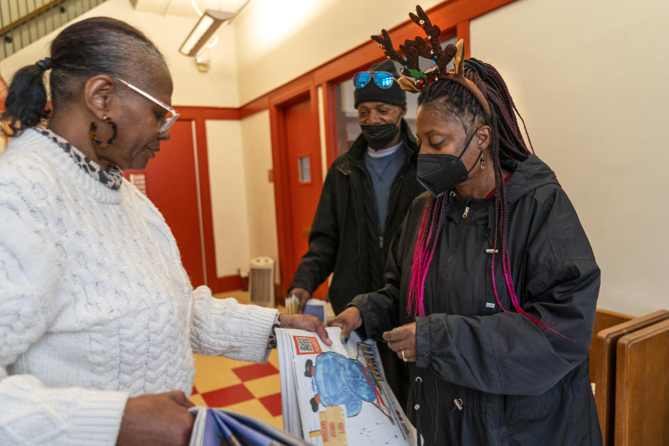 Tonya Williams, right, a vendor who sells street Sense, a local paper that covers issues related to the homeless and employs unhoused individuals as its vendors, gets more papers to sell from Street Sense staff member Aida Peery, left, Wednesday, Dec. 6, 2023, in Washington. The transition to a cashless society has impacted street-level charitable giving – from individual donations to panhandlers to the Salvation Army donation kettles. Street Sense vendors now accept donations from cashless apps like Venmo and CashApp. (AP Photo/Jacquelyn Martin)