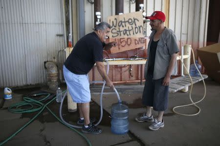 Pastor Frankie Olmedo, 56, (L) who volunteers four hours a day to hand out water, fills up a container for Luis Bocanegra, 35, in Porterville, California October 14, 2014. REUTERS/Lucy Nicholson