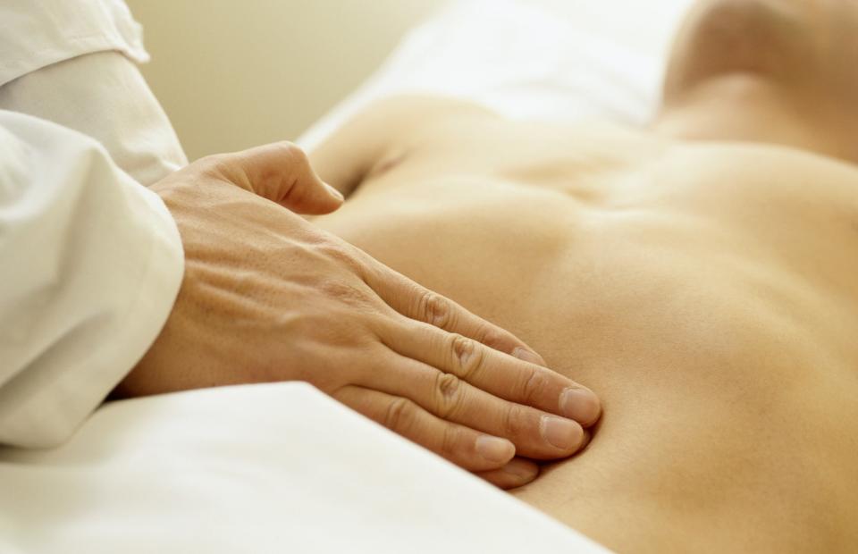 A person lying down receives a physical examination as the doctor's hand gently presses their abdomen