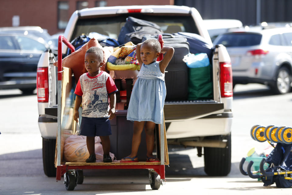 Youngsters wait on a luggage cart as the belongings of African asylum seekers are packed onto moving trucks at the Portland Expo, Thursday, Aug. 15, 2019, in Portland, Maine. The state's largest city is racing to find homes for dozens of African asylum seekers as a temporary shelter closes on Thursday. (AP Photo/Robert F. Bukaty)