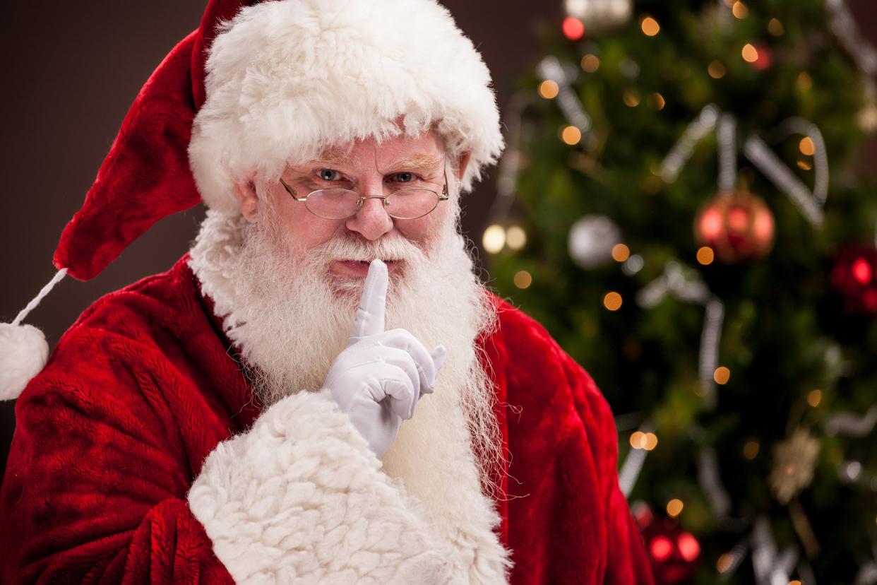 Santa Claus with finger to lips with Christmas tree in background