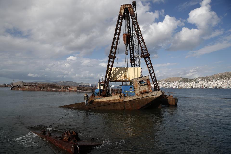 A floating crane holds an old vessel as a worker checks the progress of shipwreck raising operation on Salamina island, west of Athens, on Friday, Nov. 8, 2019. Greece this year is commemorating one of the greatest naval battles in ancient history at Salamis, where the invading Persian navy suffered a heavy defeat 2,500 years ago. But before the celebrations can start in earnest, authorities and private donors are leaning into a massive decluttering operation. They are clearing the coastline of dozens of sunken and partially sunken cargo ships, sailboats and other abandoned vessels. (AP Photo/Thanassis Stavrakis)