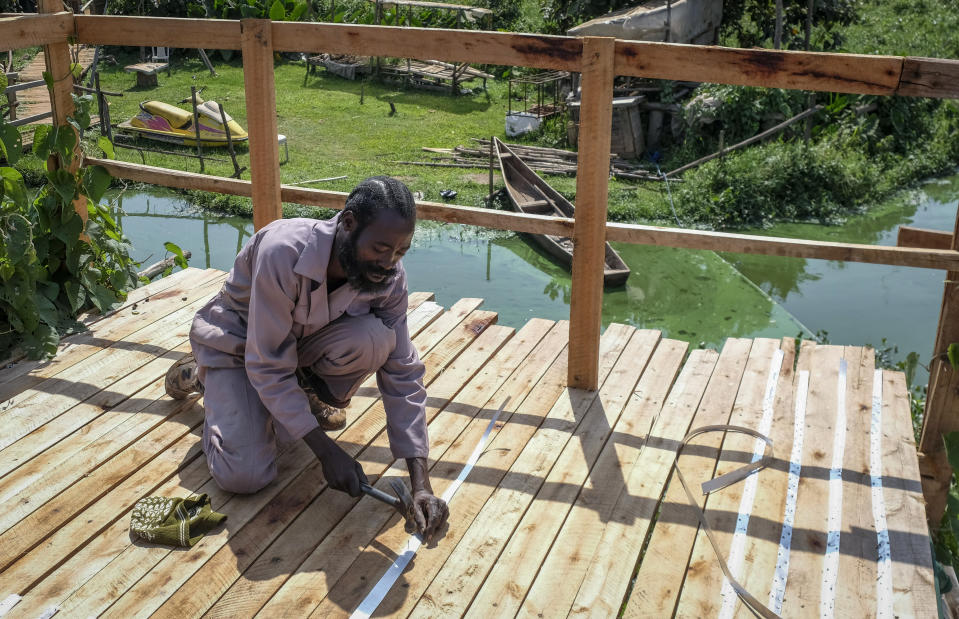 A worker performs renovations on the structure of a floating restaurant and bar, on Lake Victoria near the Luzira area of Kampala, Uganda Sunday, Feb. 19, 2023. Flowering plants rise from the water into the wooden hull of James Kateeba's boat, used as a floating restaurant and bar that can be unmoored to drift for pleasure, but the greenery emerges from an innovative recycling project which uses thousands of dirt-encrusted plastic bottles to anchor the boat. (AP Photo/Hajarah Nalwadda)