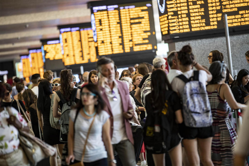 Passengers gather beneath display boards showing train times at Termini station in Rome, Monday, July 22, 2019. A suspected arson fire has forced cancellations of at least 42 high-speed trains in Italy on the heavily-traveled Milan-Naples corridor. (Massimo Percossi/ANSA via AP)