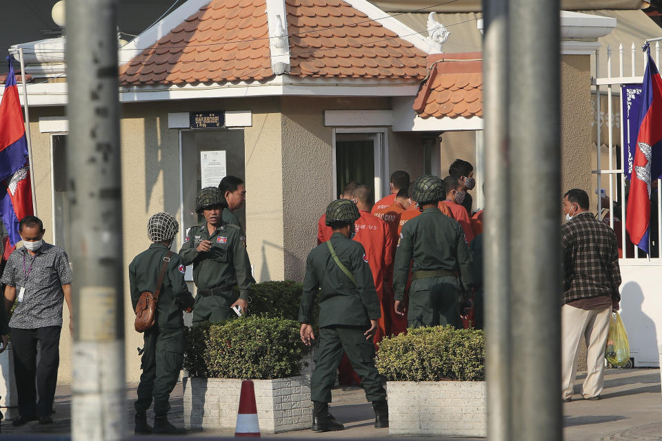 Cambodian police officers escort prisoners, in orange clothes, including Rong Chhun, president of the Cambodian Confederation of Unions, as they enter the Phnom Penh Municipal Court in Phnom Penh, Cambodia Friday, Jan. 15, 2021. The trial of the Cambodian labor union leader charged with inciting social unrest opened Friday, part of a large-scale legal offensive by the government against its critics. (AP Photo/Heng Sinith)