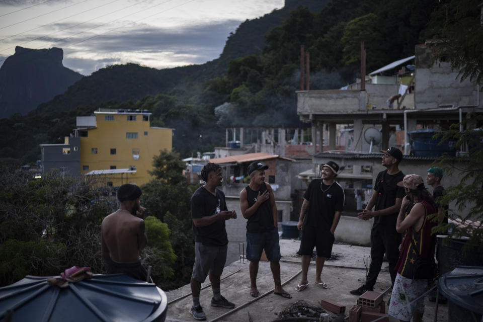 Trap de Cria artist Vitor Oliveira, known as "MC Piloto," second left, gathers on the rooftop of his home and recording studio with friends and other rappers in the Rocinha slum of Rio de Janeiro, Brazil, Thursday, March 18, 2021. Oliveira is churning out a new type of music, Trap de Cria, which roughly translates into Homegrown Trap, and planning a blitz of 18 original tracks, all accompanied by videos. (AP Photo/Felipe Dana)