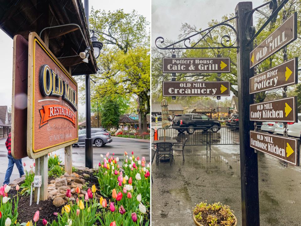Left: a brown sign with pink, red, and yellow tulips below it and trees in the background. Right: A back pole with brown signs for shops and restaurants sticking out of it and trees in the background. Thee sky is gray.