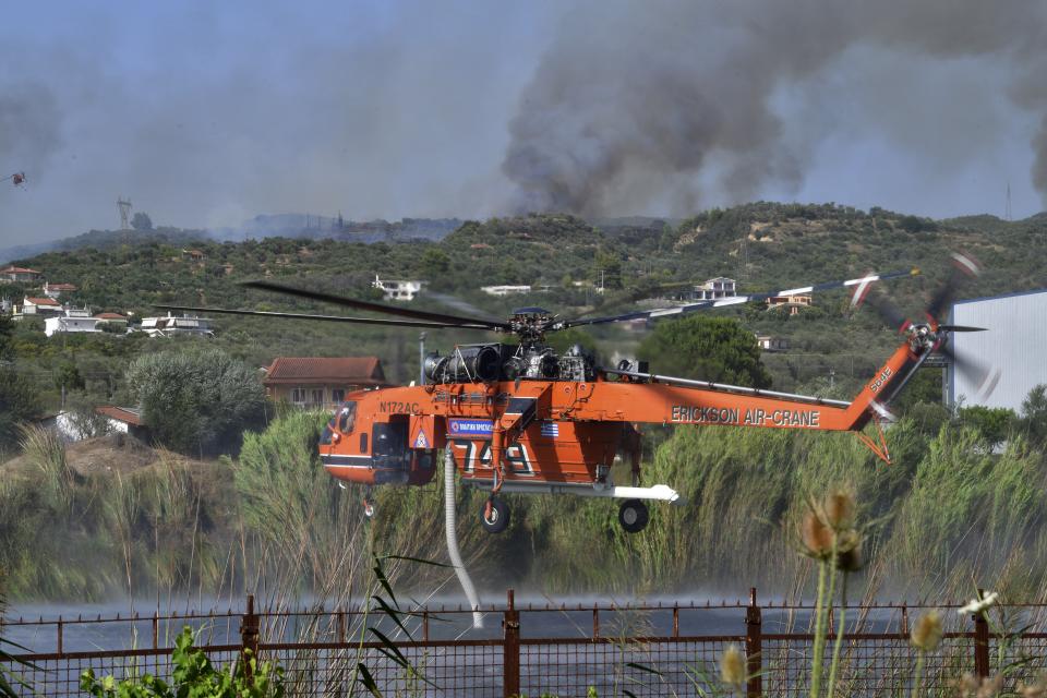 An helicopter fills water during a wildfire near Pyrgos town, western Greece, Thursday, Aug. 5, 2021. Wildfires rekindled outside Athens and forced more evacuations around southern Greece Thursday as weather conditions worsened and firefighters in a round-the-clock battle stopped the flames just outside the birthplace of the ancient Olympics. (Giannis Spyrounis/ilialive.gr via AP)