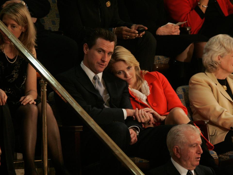 Jennifer Siebel Newsom and Gavin Newsom snuggle while watching a political ceremony.