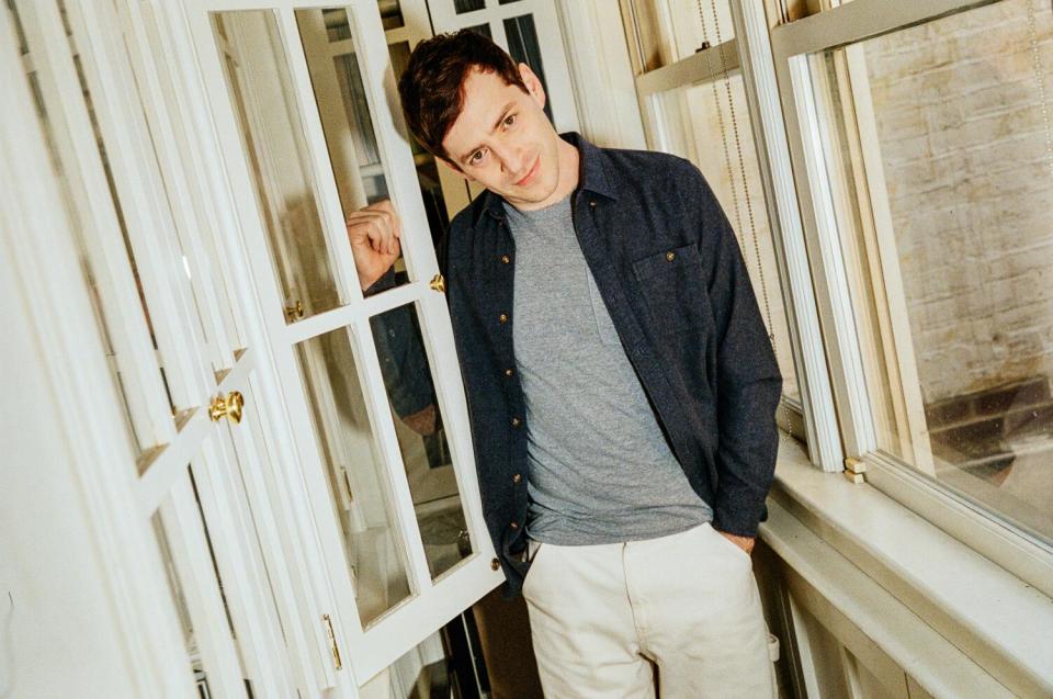 A man poses for the camera between a book cabinet and a window.