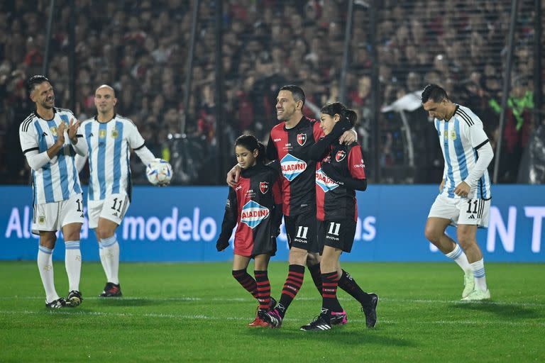 Aplaudido por Martín Demichelis, Maximiliano Rodríguez abraza a sus hijas Alma y Aitana, que jugaron una parte del partido de despedida de su papá.