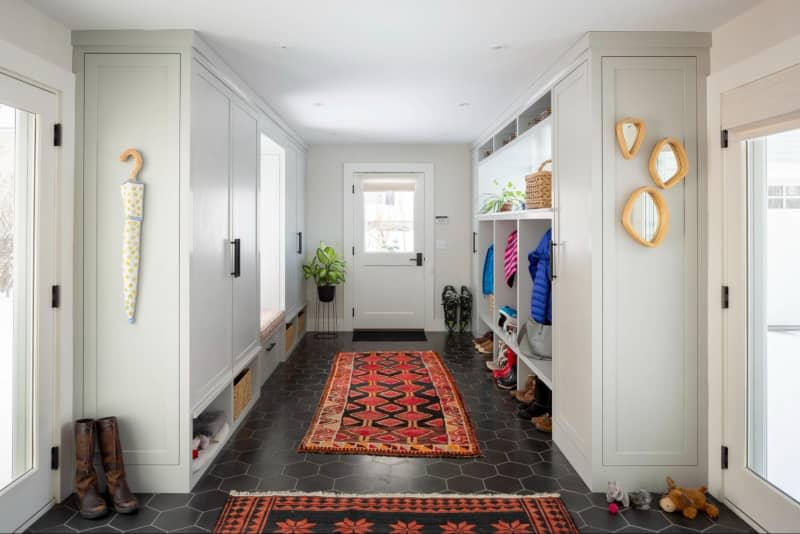 White entry way with dark tile floors and red vintage runners, built in cubbies for boots and coats