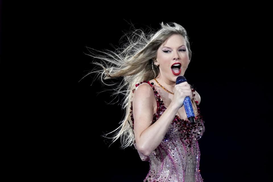 Taylor Swift singing with a mic to her mouth against a dark backdrop