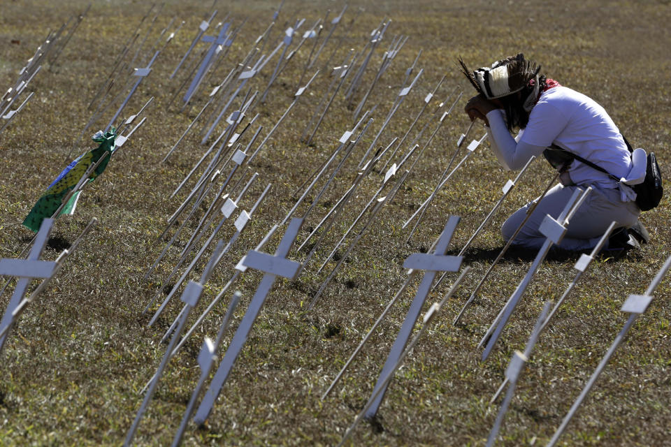 A demonstrator kneels before rows of crosses representing the thousands of deaths due to the new coronavirus, during a protest demanding President Jair Bolsonaro be impeached, in front of the National Congress in Brasilia, Brazil, Tuesday, July 14, 2020. As Brazil careens toward a full-blown public health emergency and economic meltdown, opponents have filed a request for Bolsonaro's impeachment based on his mishandling of the new coronavirus pandemic. (AP Photo/Eraldo Peres)